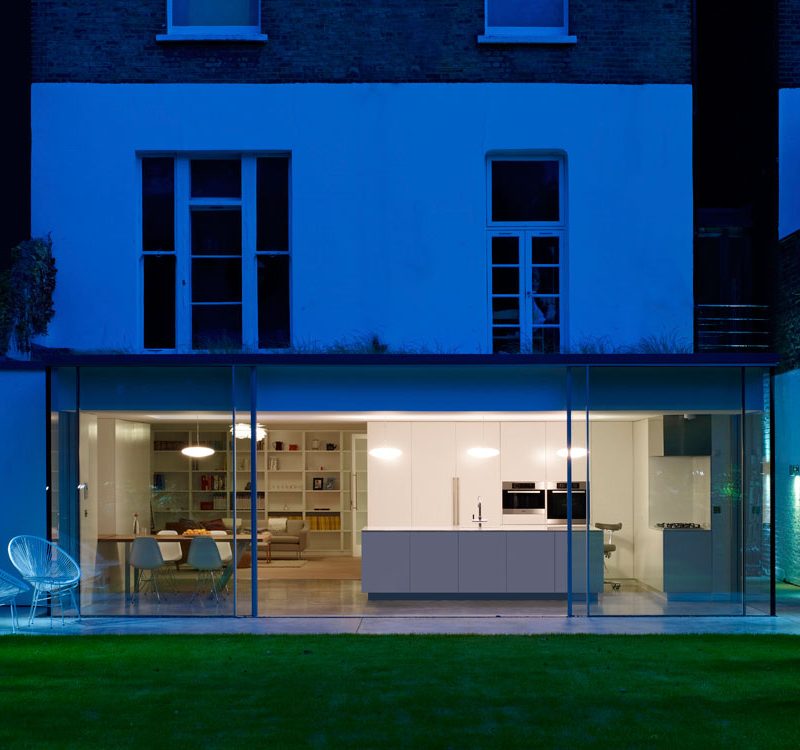 Modern kitchen extension at night with full glazing, by Nationserv